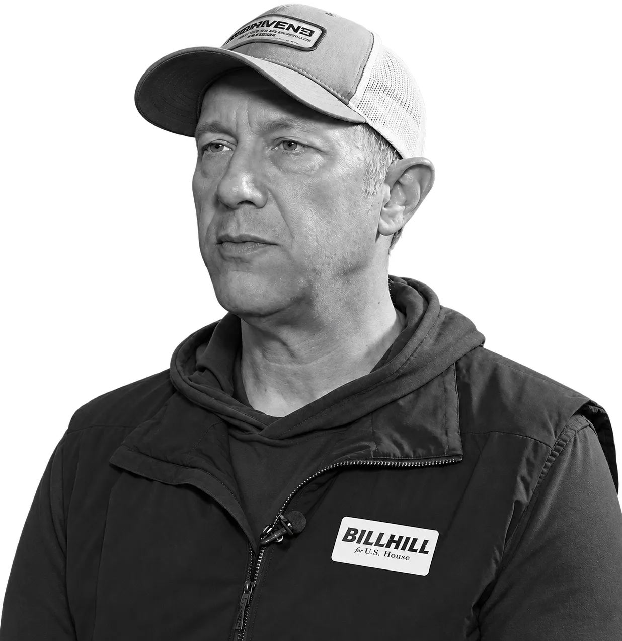 Bill Hill, photographed outdoors in a trucker cap and a black puffer vest with a 'BILLHILL for U.S. House' campaign badge.